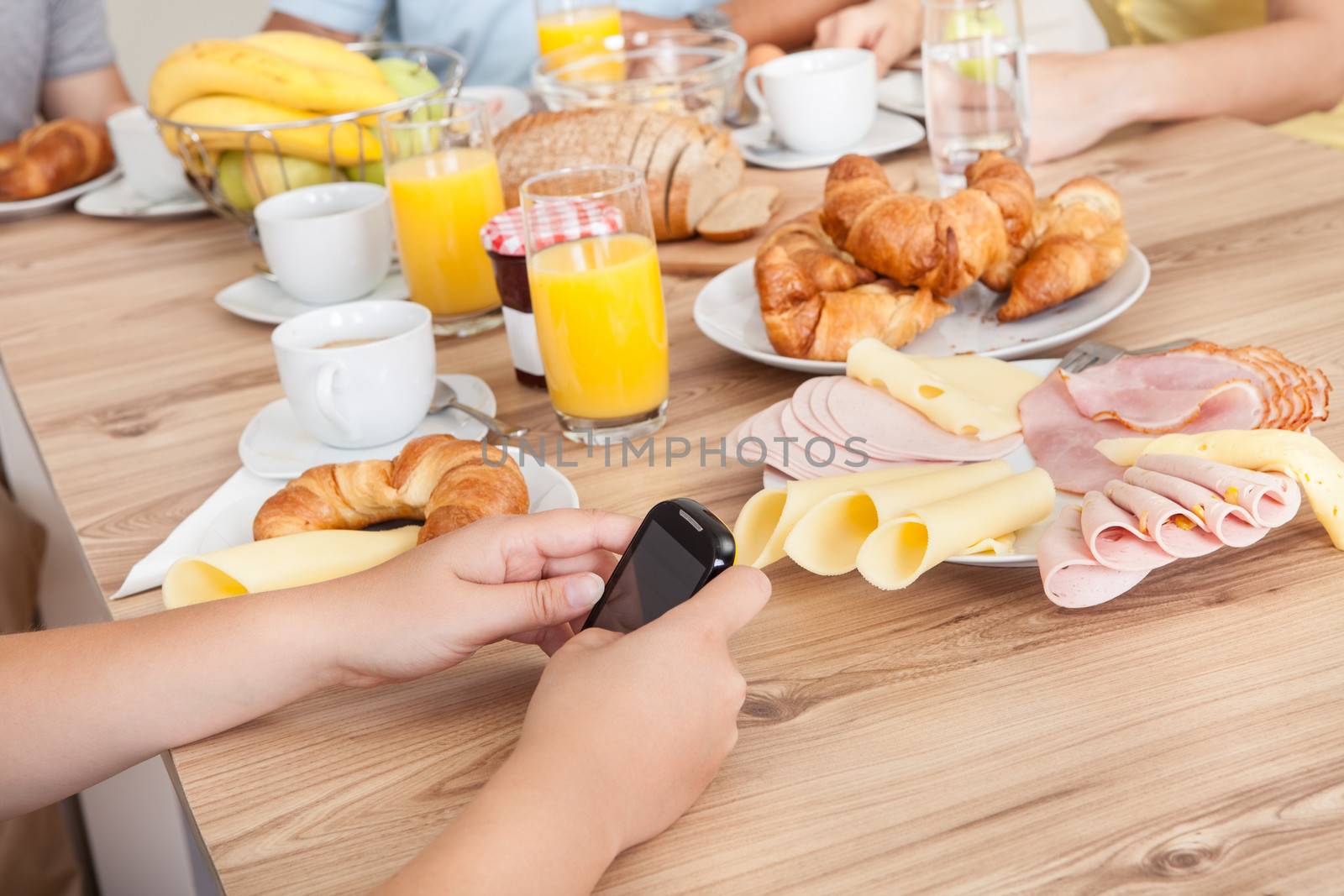 Close-up on teenager texting on her mobile phone in the kitchen while the rest of the family enjoy breakfast