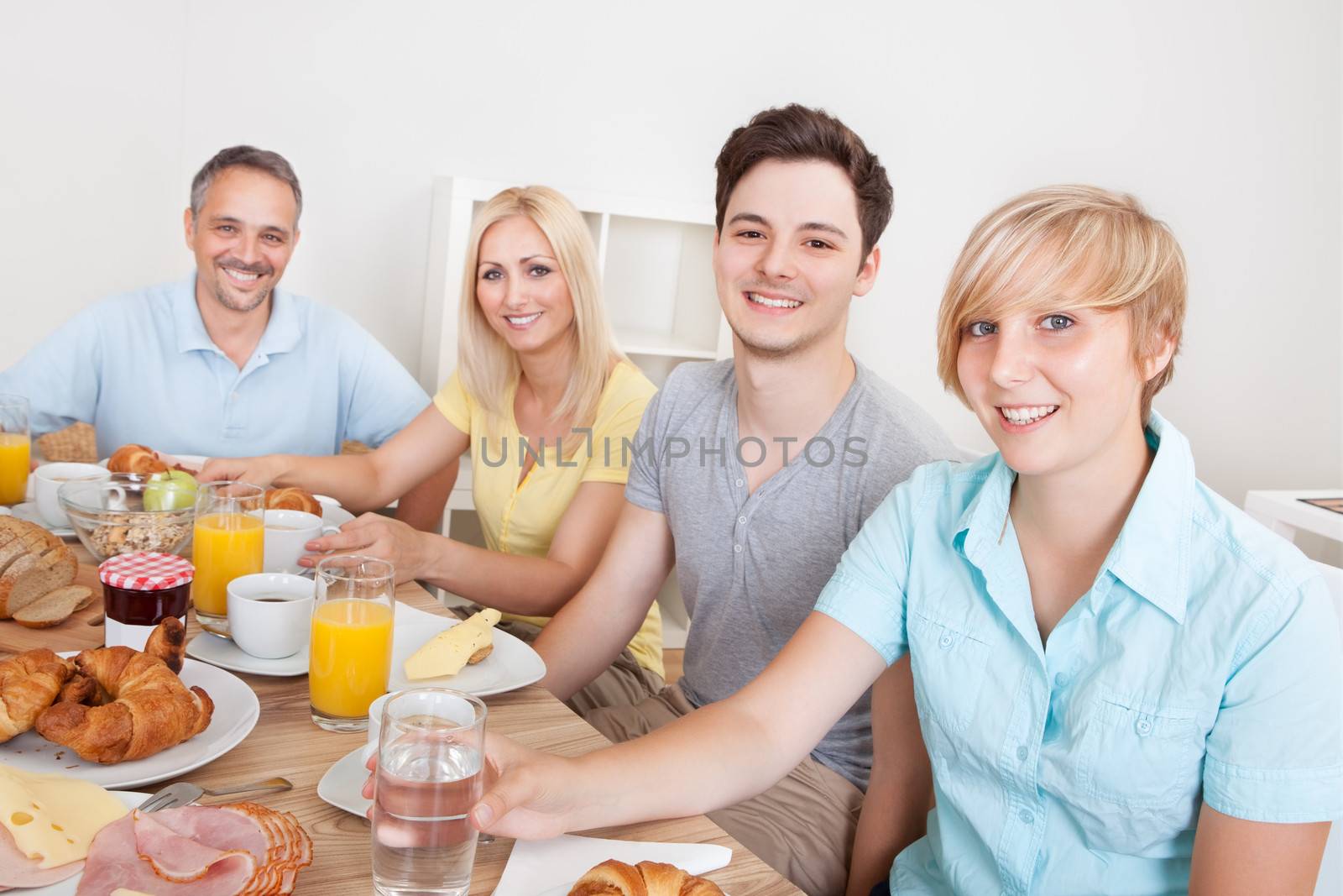 Happy family with two teenage children sitting around the table enjoying a healthy breakfast