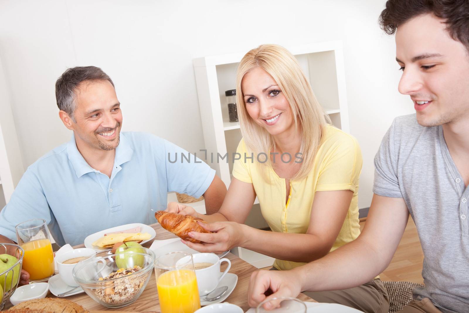 Happy family with two teenage children sitting around the table enjoying a healthy breakfast
