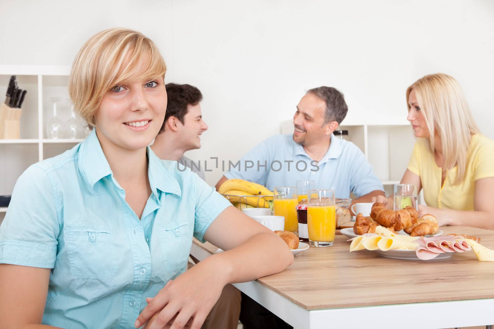 Attractive teenage girl sitting in the foreground with her family seated at the table in front of a large healthy breakfast