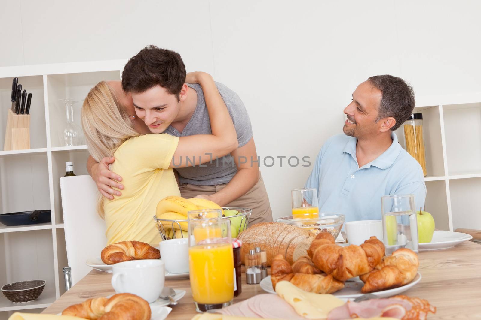Mother and son enjoy a hug at the breakfast table watched by the happy proud father