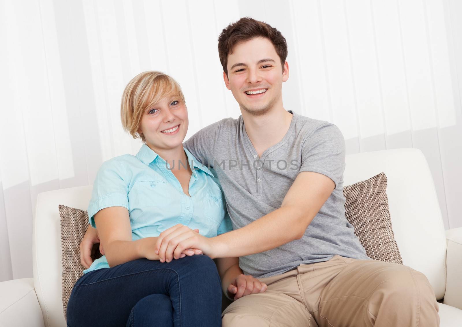 Smiling loving attractive young couple sitting close together relaxing on a sofa