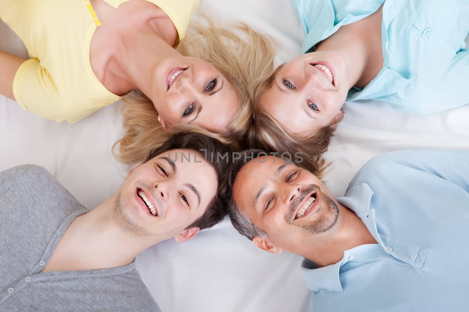 Joyful family lying in a circle on their backs looking up at the camera with their heads close together