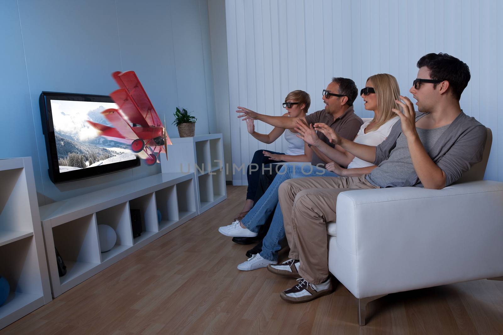 Conceptual image of a family watching 3D television and stretching out their hands as though to touch the image on the screen