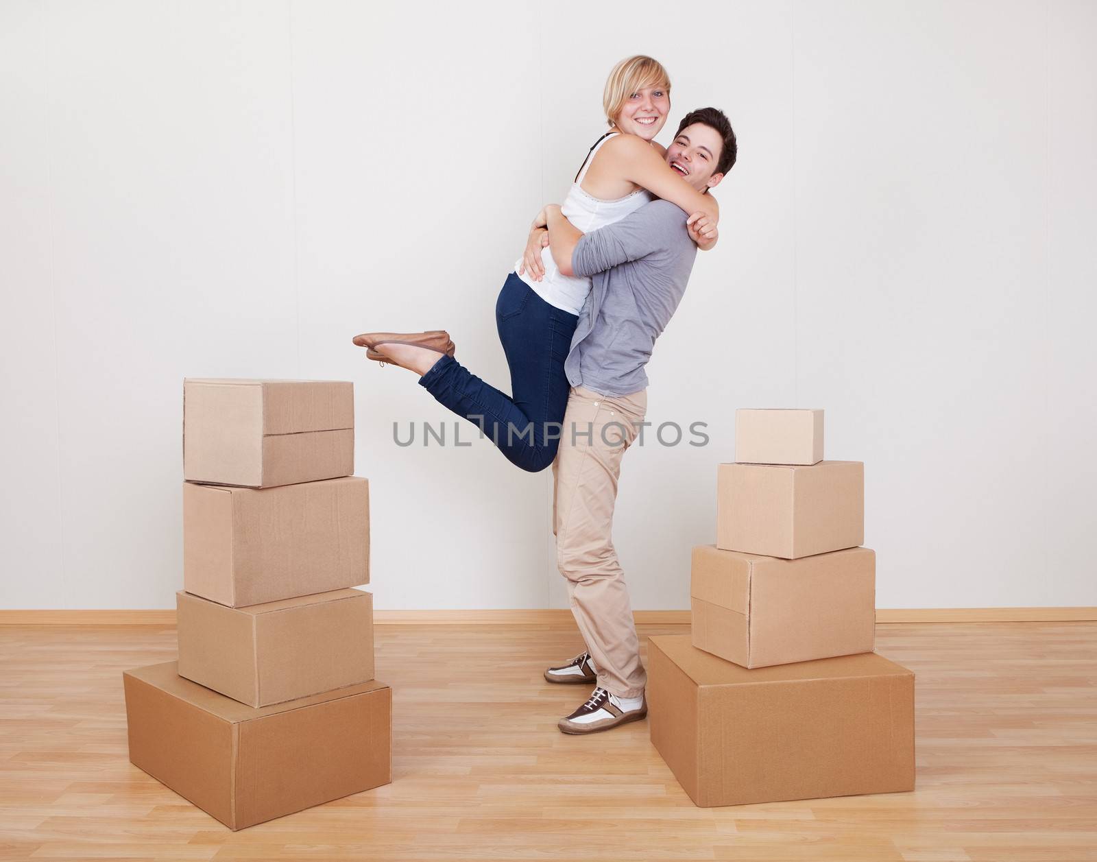 Happy young couple in a close ecstatic embrace smiling happily as they stand surrounded by cartons in their new home
