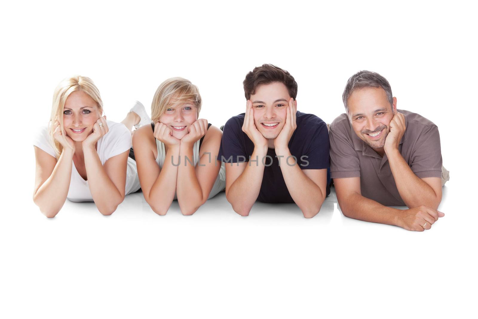 Happy friendly family with a teenage son and daughter lying in a row on the floor on their stomachs relaxing resting on their elbows