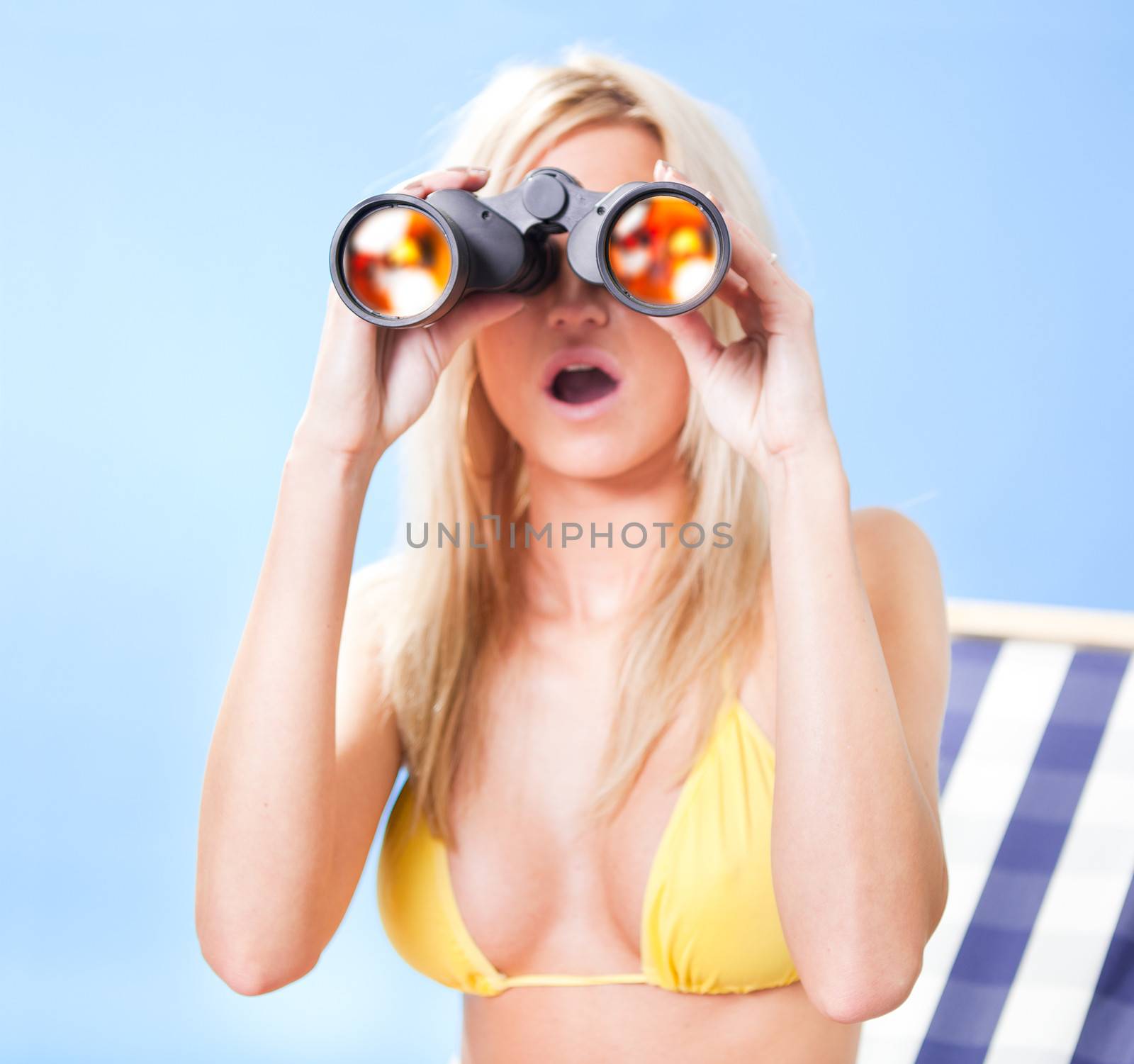 Beautiful young woman in bikini lying on a deckchair looking through binoculars at the beach