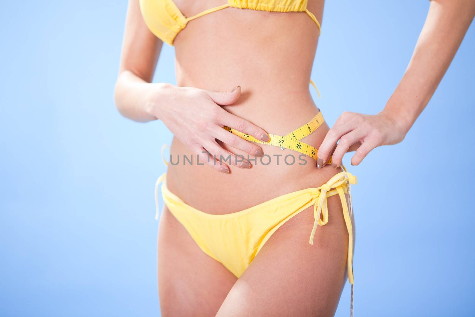 Beautiful young woman in bikini measuring waist at the beach