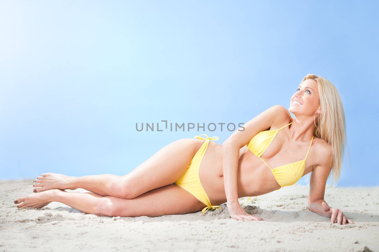 Beautiful young woman in bikini lying on the send at the beach