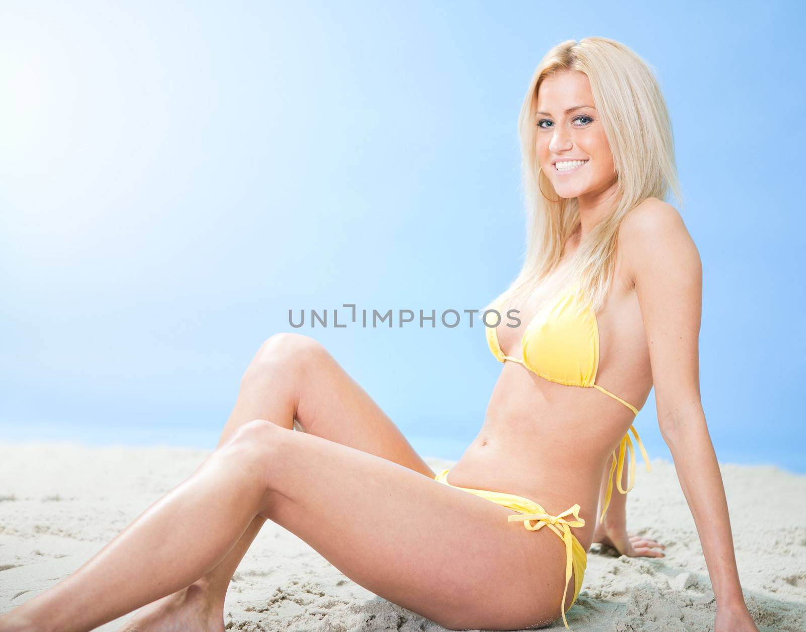 Beautiful young woman in bikini sitting on the send at the beach