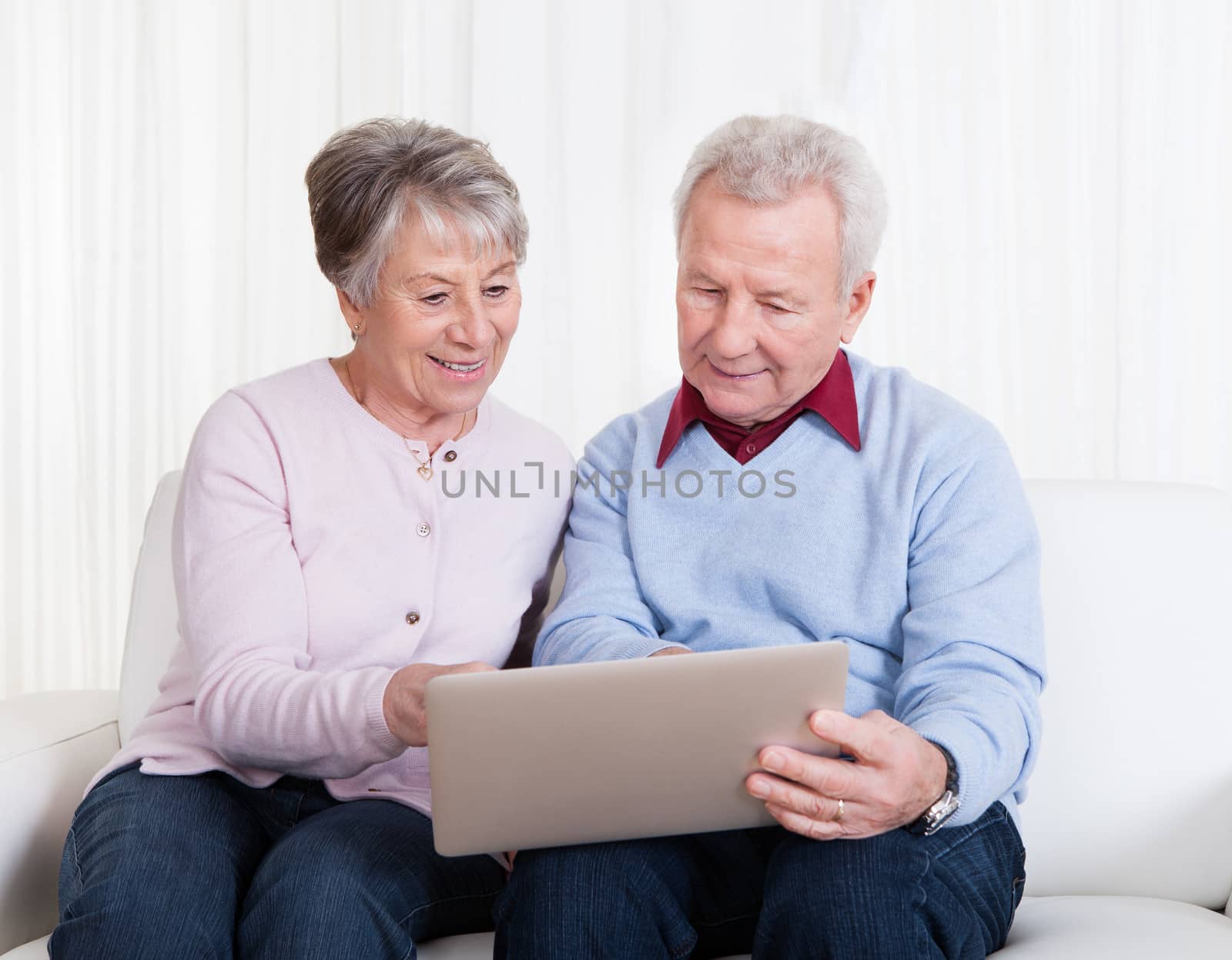 Senior Couple Sitting On Couch And Looking At Laptop Computer