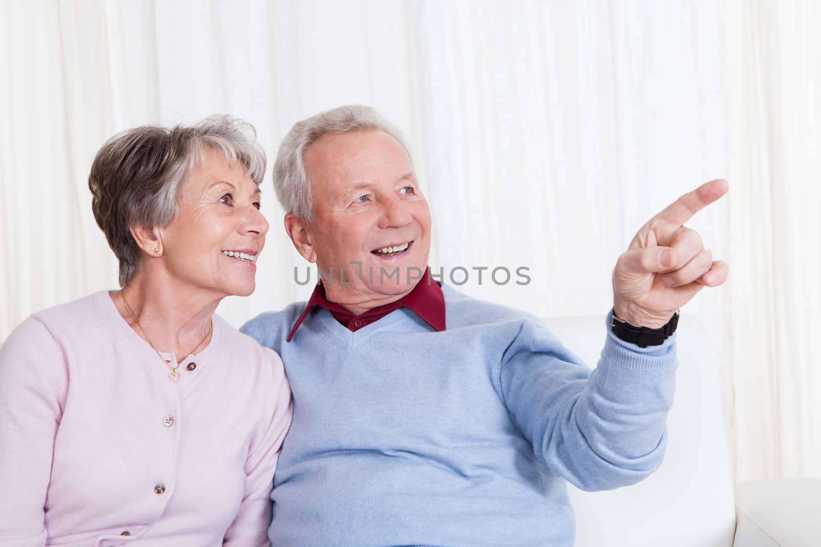 Portrait Of Happy Senior Couple Gesturing And Sitting On Couch