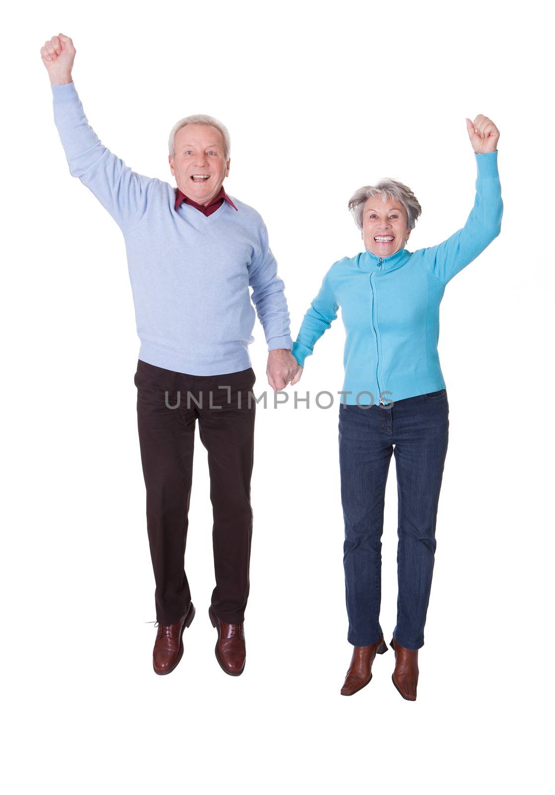 Portrait Of Senior Couple Jumping In Joy Over White Background