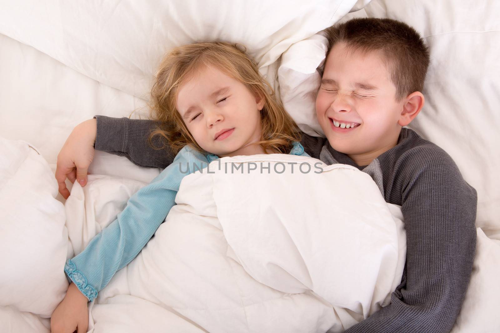 Two cute young children sleeping together sharing the same bed with a little boy protectively, cuddling his younger sister
