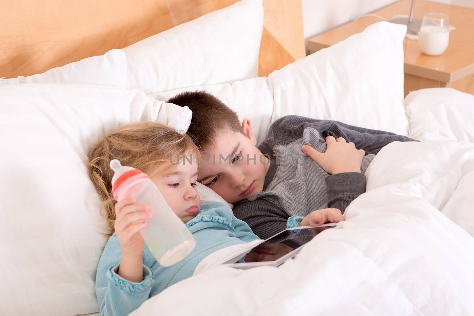 Tired little brother and sister going to sleep lying close together in a warm comfortable bed with a tablet computer on which they have just read a bedtime story