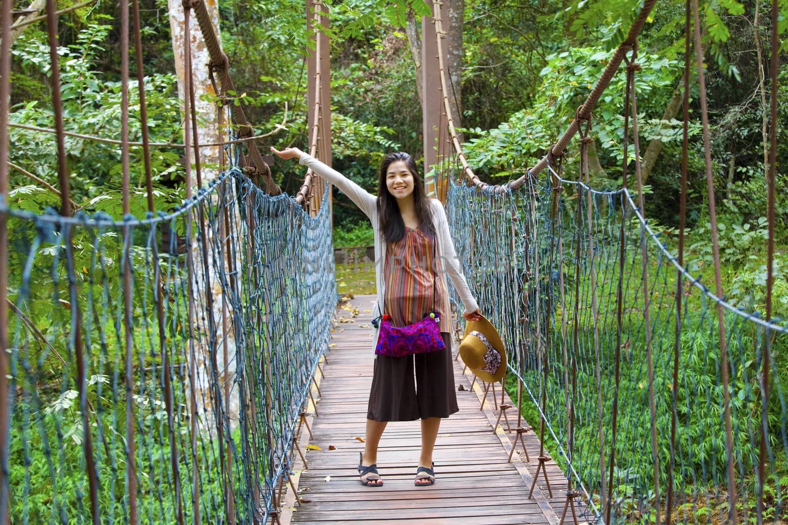 Biracial teen girl waving arm on wooden hanging bridge