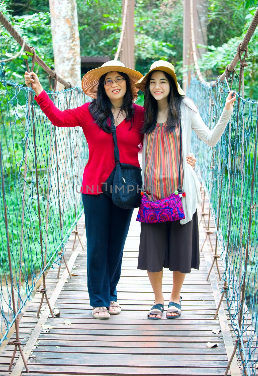 Asian mother and daughter standing together on wooden hanging bridge in forest