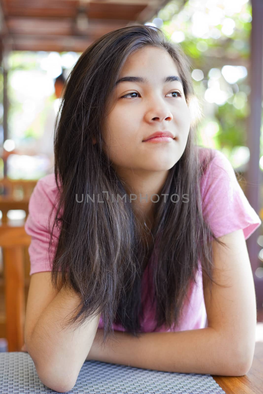 Biracial teen girl sitting at table, thinking, looking up