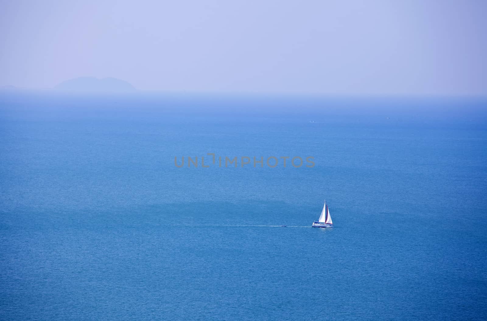 White sailboat sailing on beautiful blue ocean water, near horizon