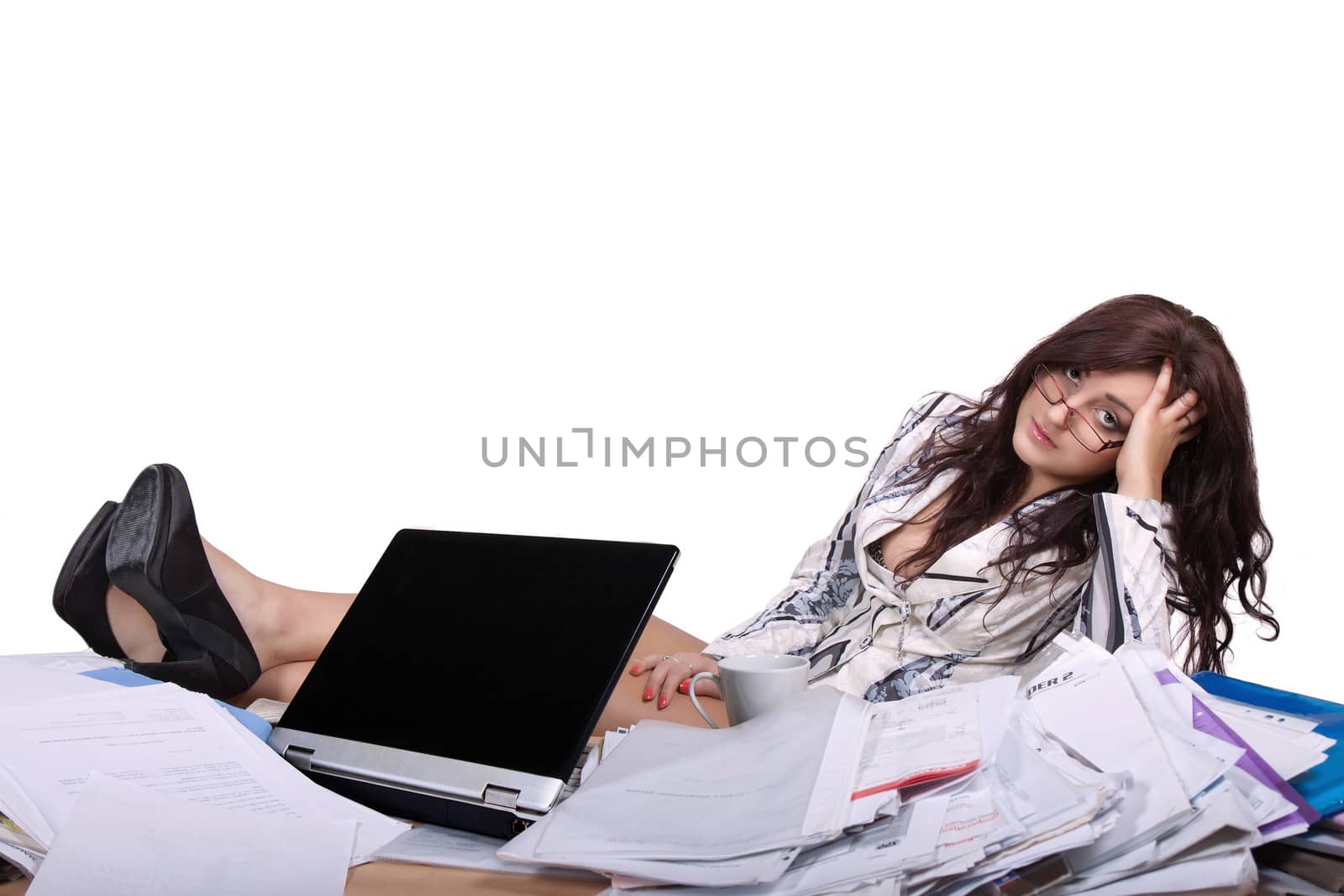 Young female office worker sitting with feet on desk with a pile of papers and looks tired and bored