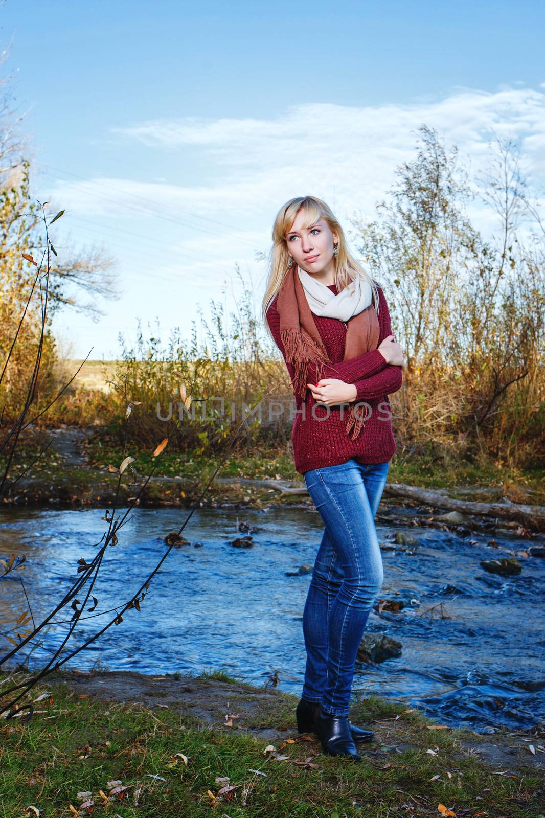 Attractive young blonde girl in sweater on alone bank of river