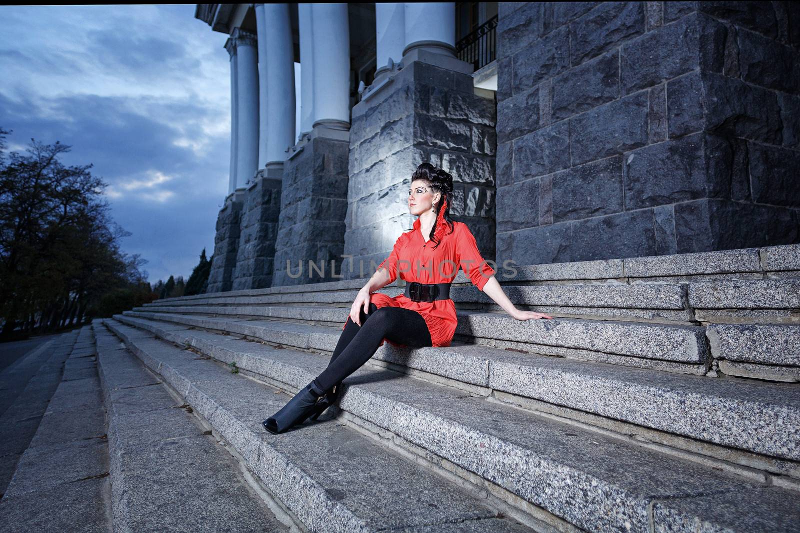 Attractive young girl with bright make-up sitting on the steps at twilight
