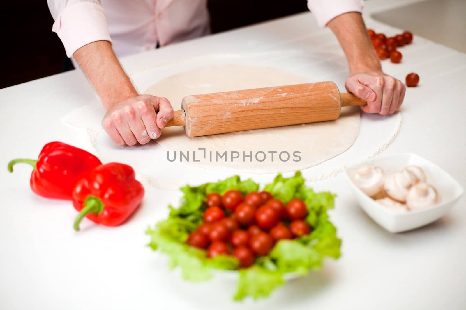 Chef is rolling dough for a italian pizza with pepperoni and mushrooms