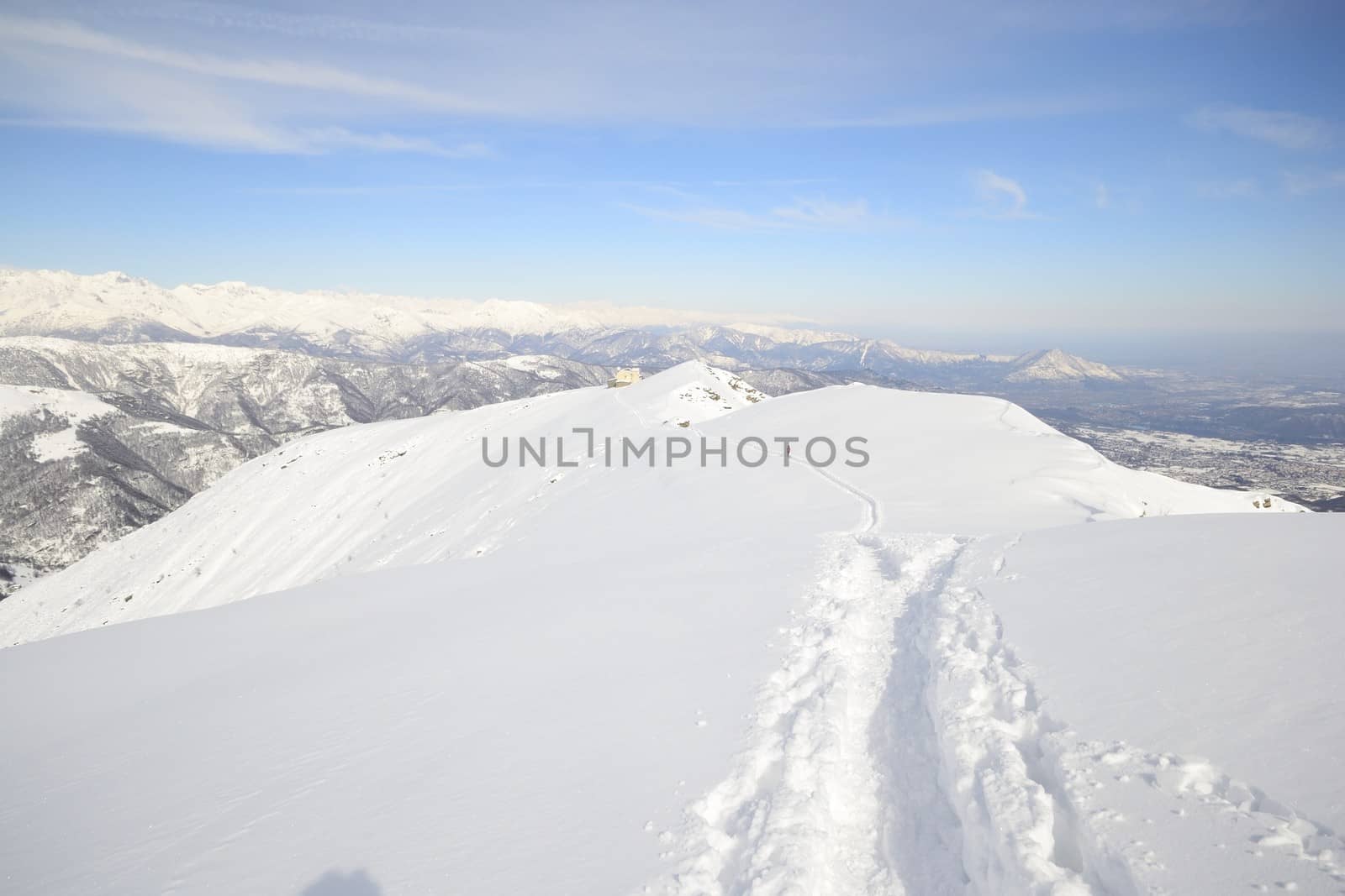 Alpinist hiking uphill by ski touring on the mountain ridge in powder snow with deep track in the foreground and scenic high mountain view in the background