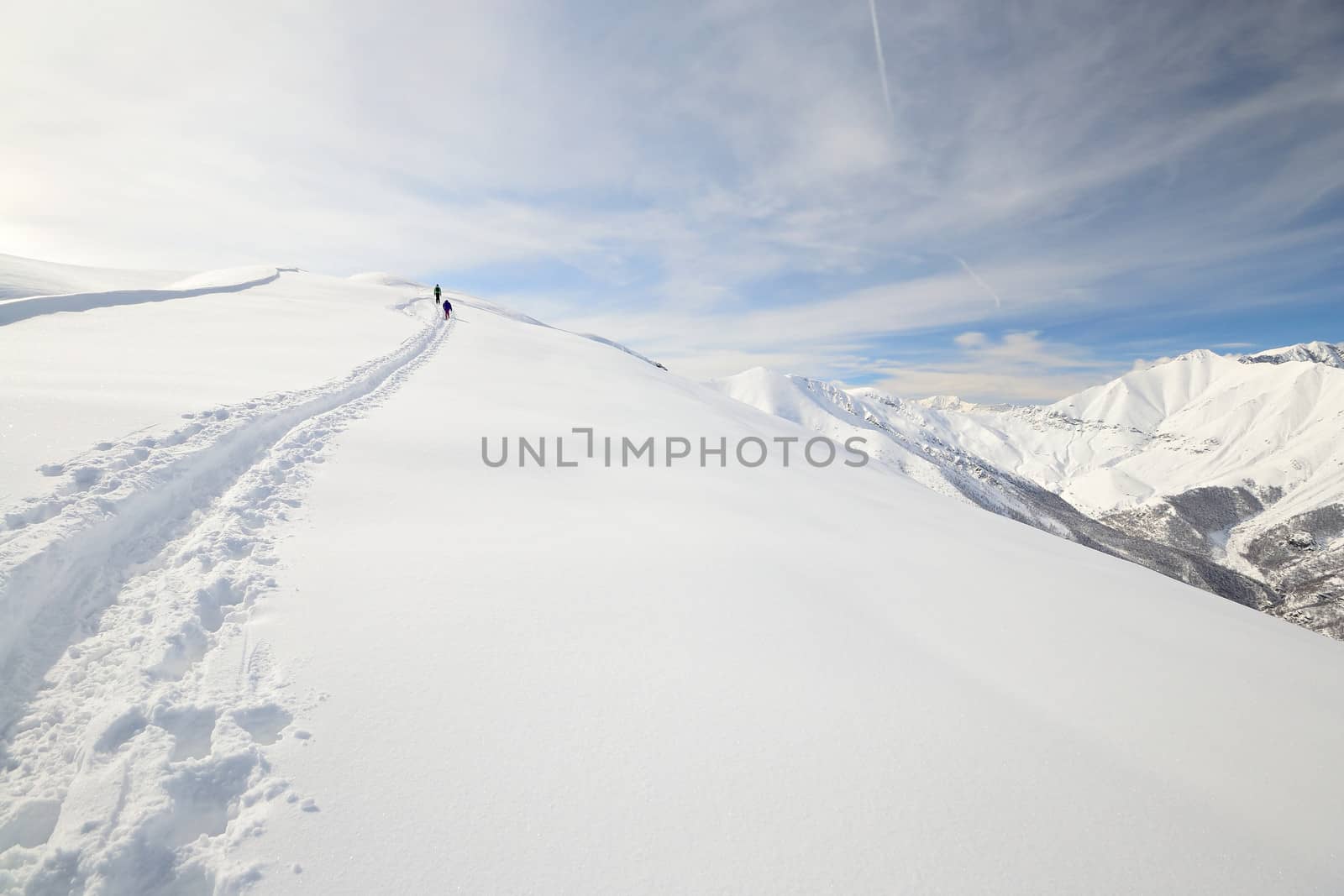 Alpinist hiking uphill by ski touring on the mountain ridge in powder snow with deep track in the foreground and scenic high mountain view in the background