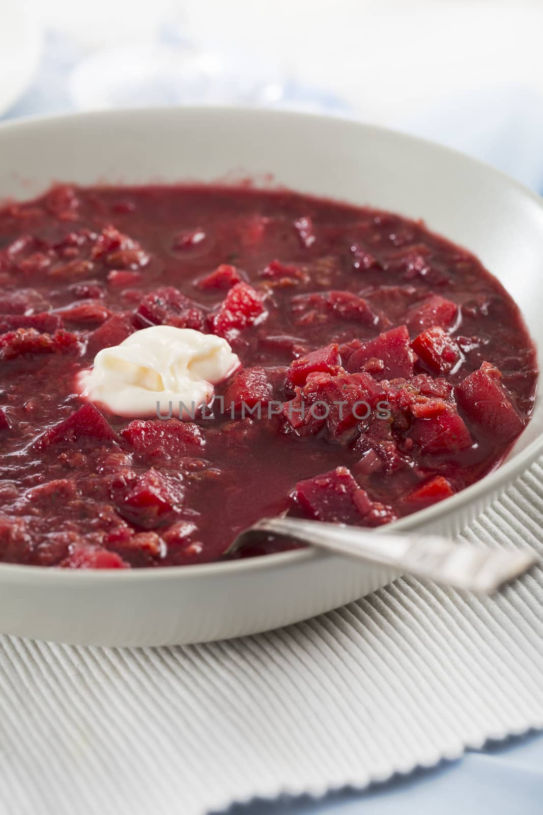 Bowl of homemade borscht soup with spoon and dollop of cream.