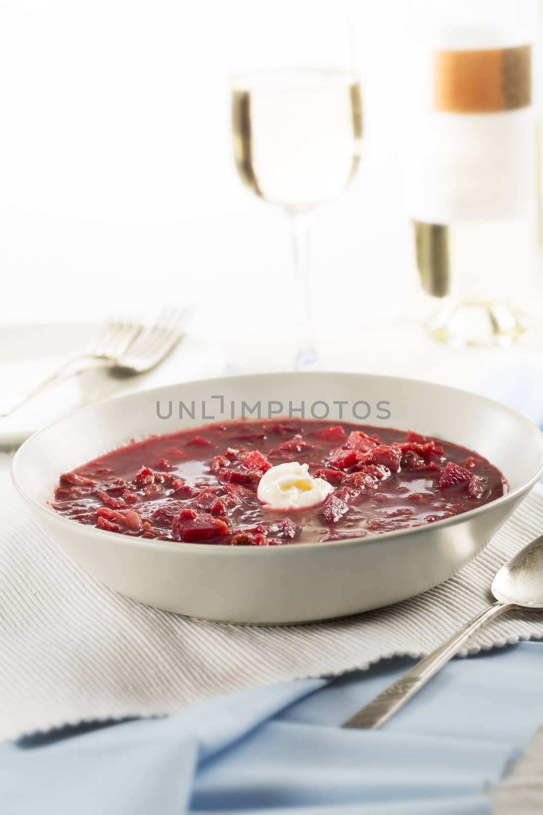Borscht on table with wine in background, vertical orientation.