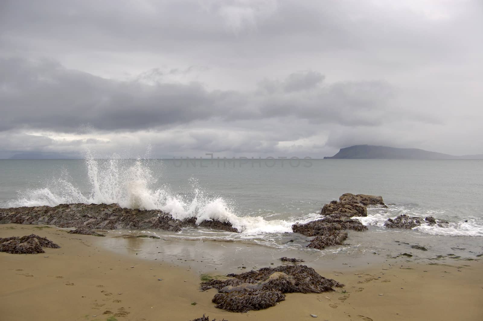 Waves crashing over rocks on a beach on the island of Rum, looking toward the island of Eigg