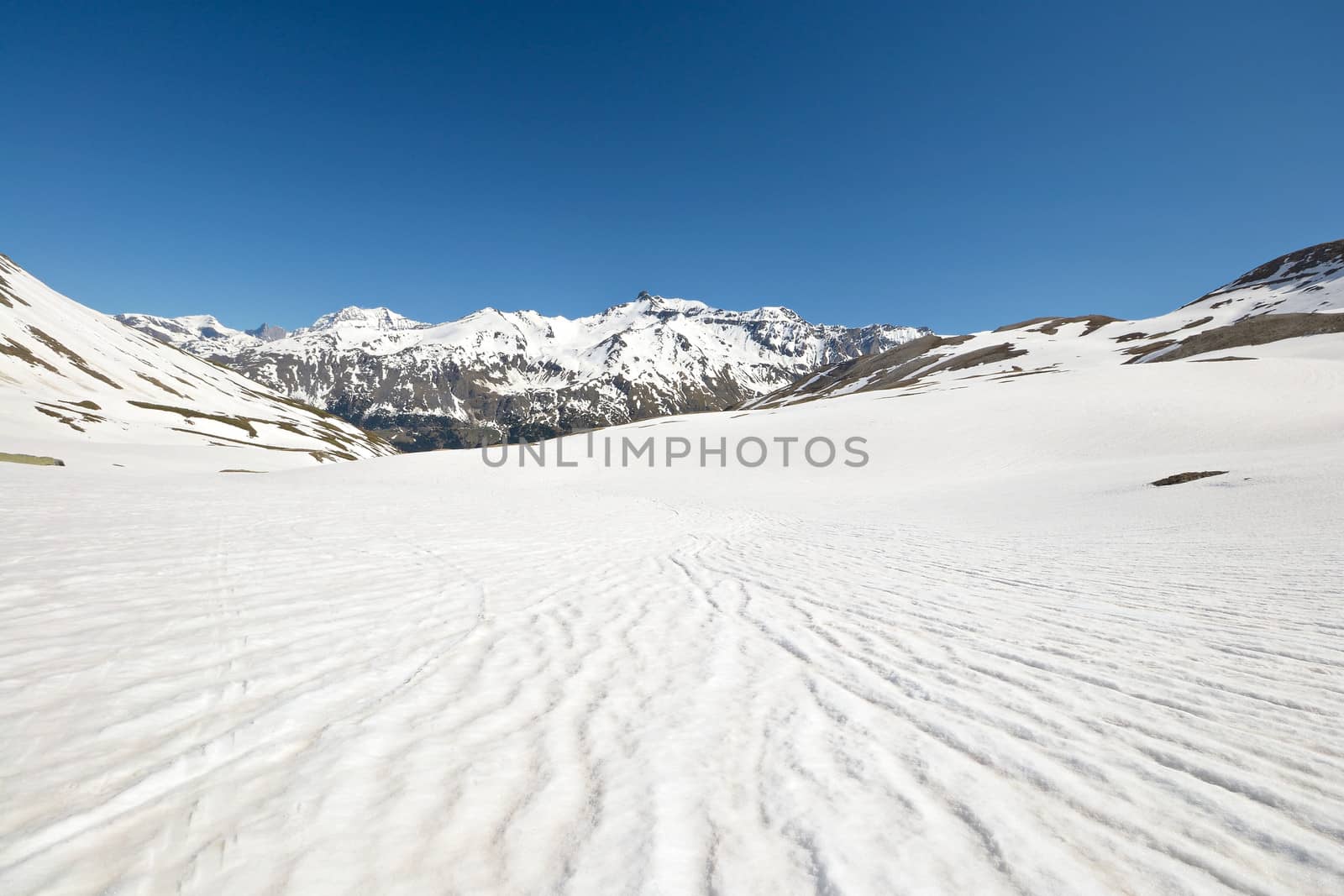 Snowy slope with melting grooves in scenic high mountain background and sunny spring day