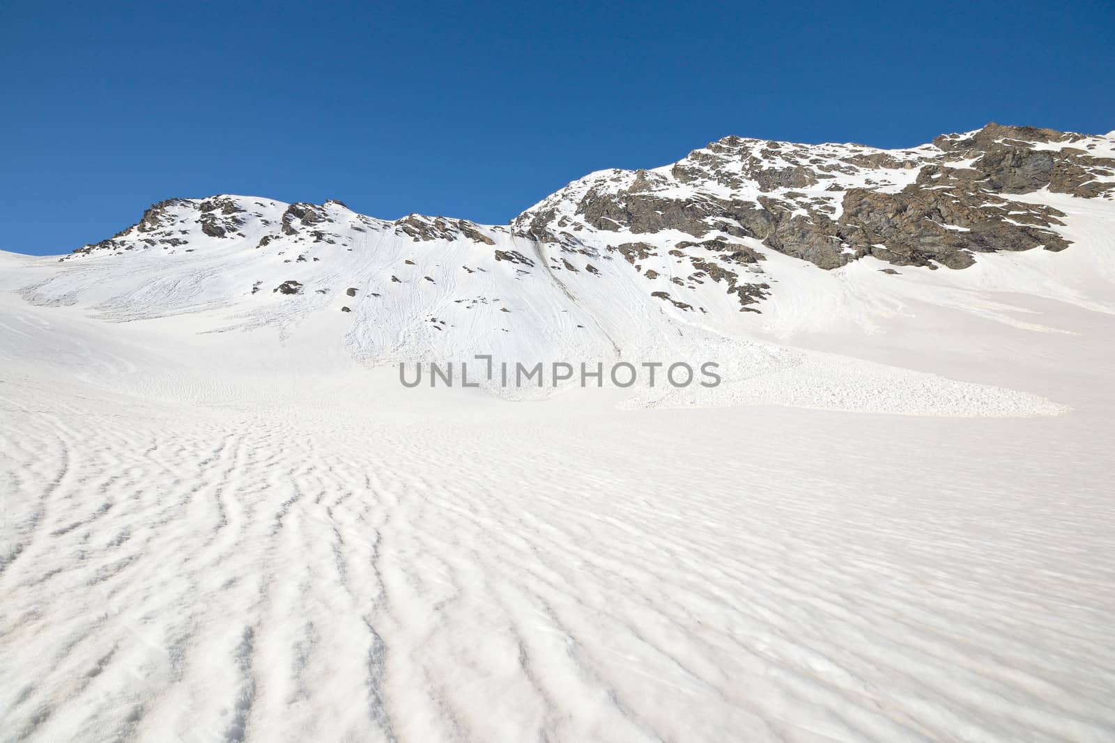 Snowy slope with melting grooves in scenic high mountain background and sunny spring day