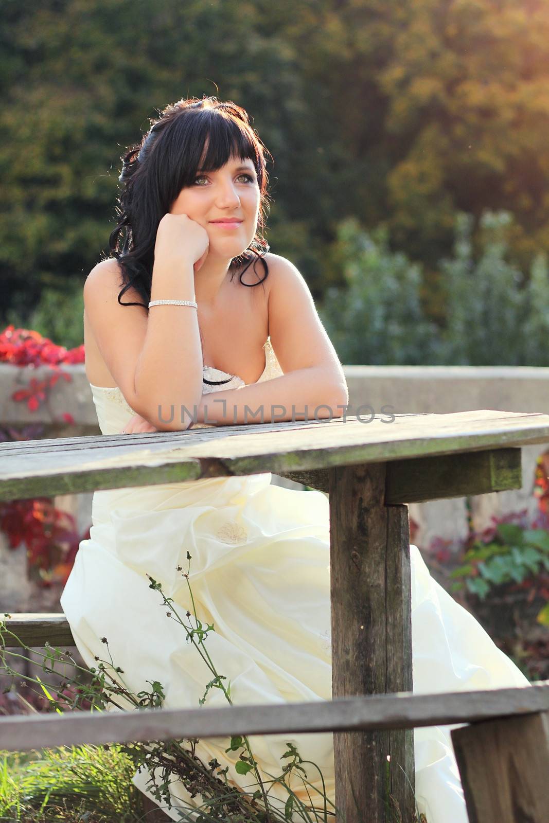 Girl in the wedding dress sitting on the bench neat the table