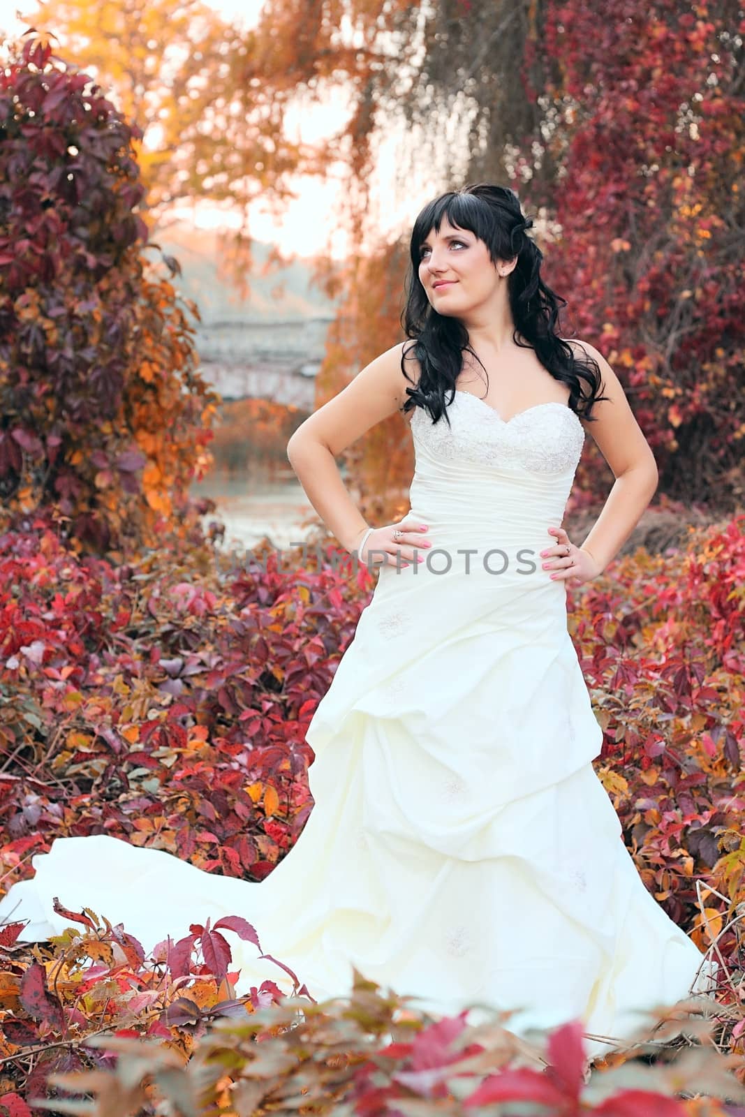 Girl in a weeding dress in a park among green and red leaves