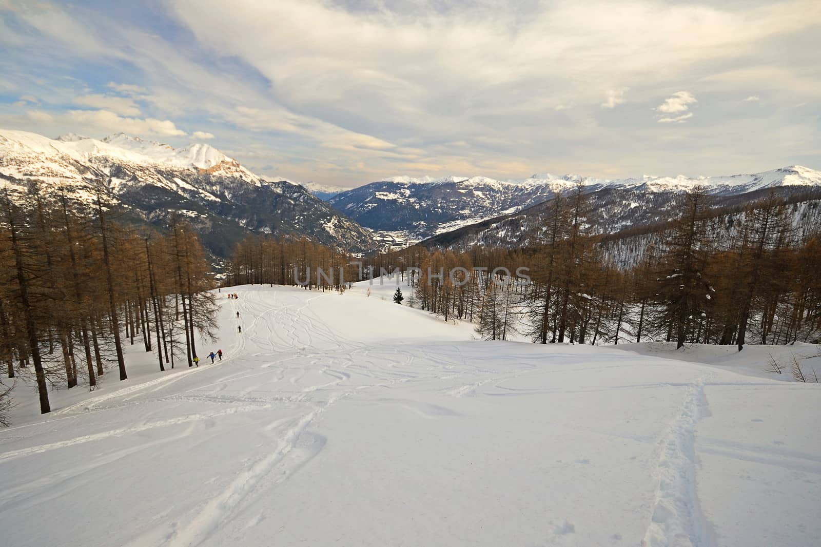 Off piste ski slope with ski tracks, some hikers and scenic valley in the italian Alps