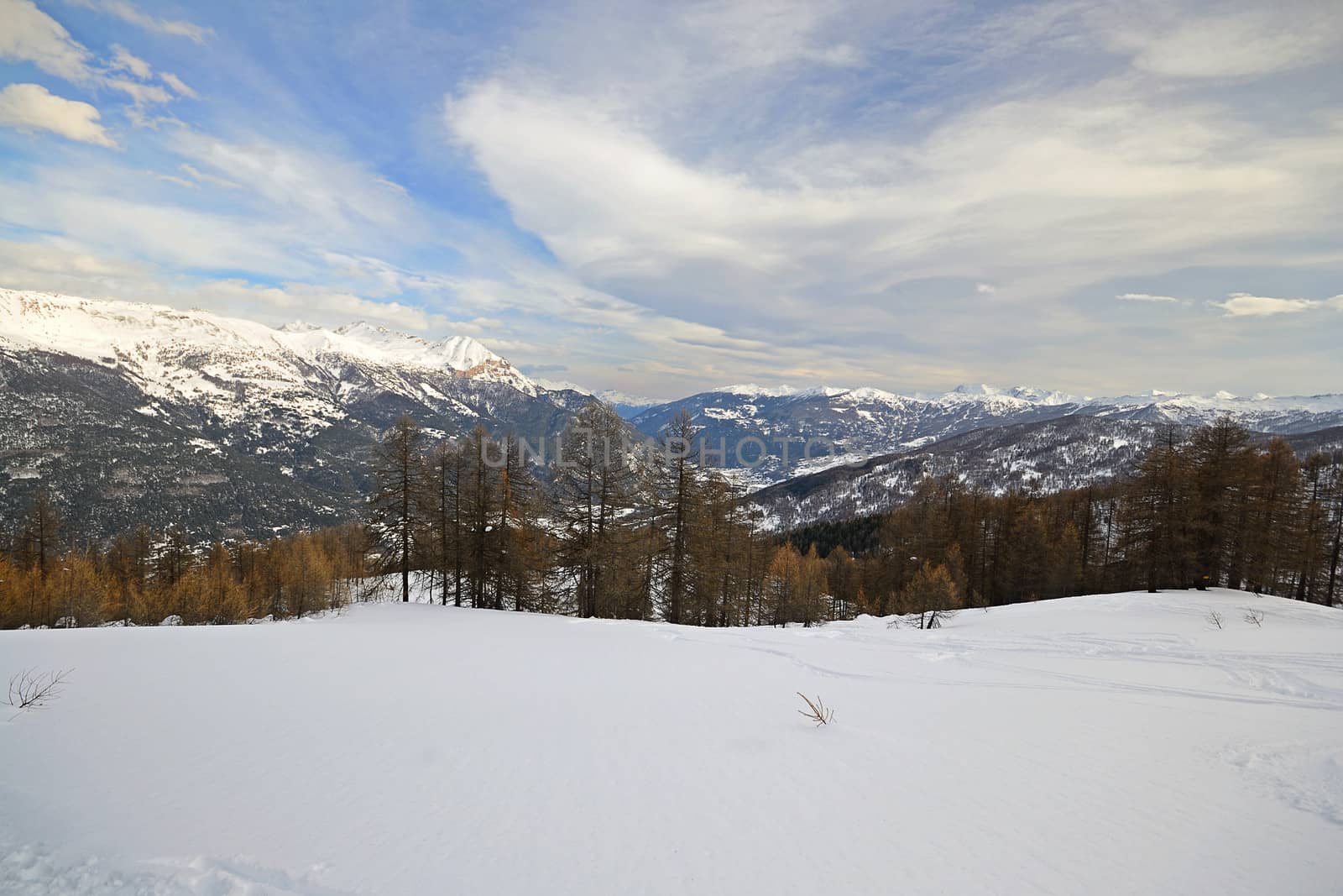 Off piste ski slope with ski tracks, some hikers and scenic valley in the italian Alps