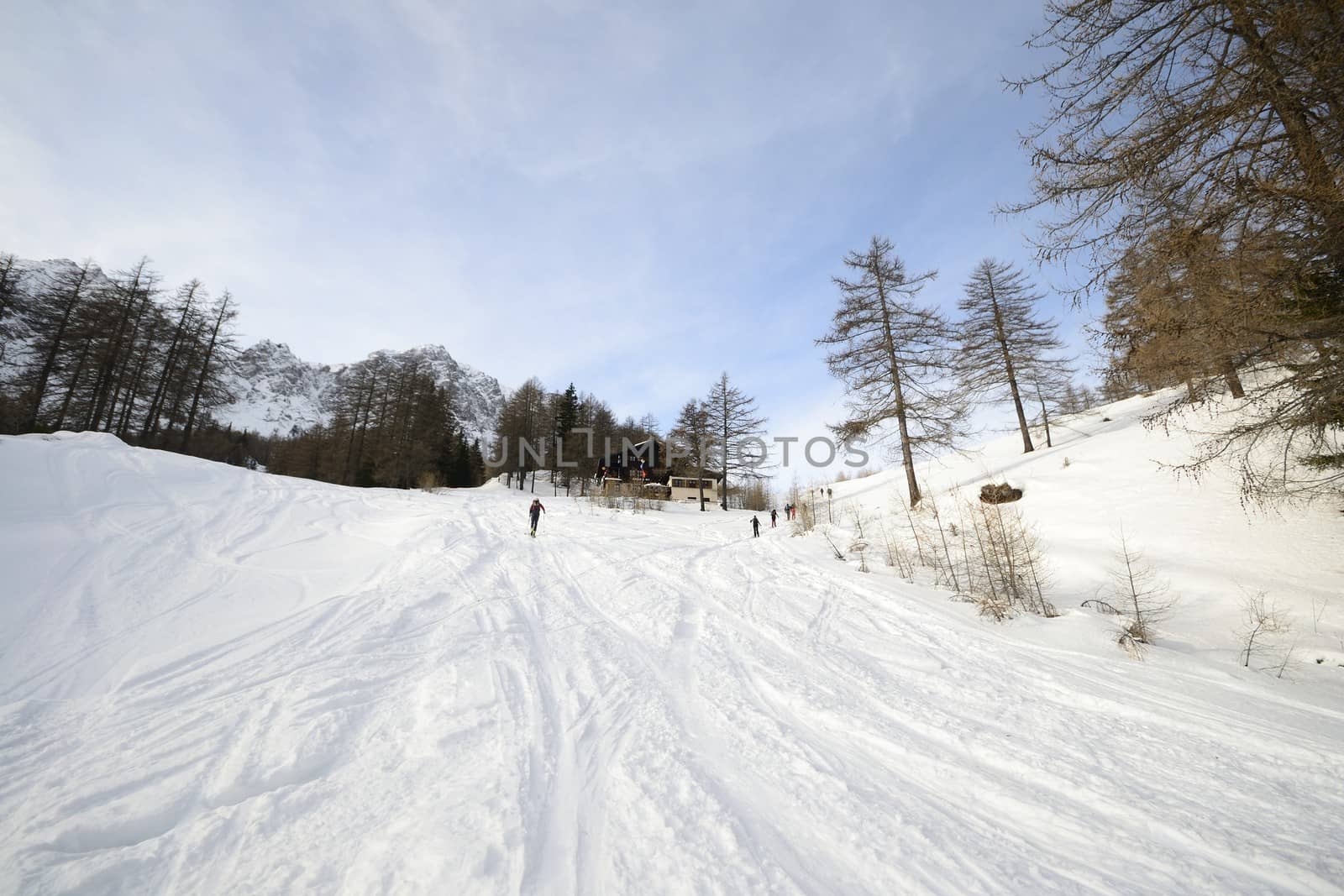 Off piste ski slope with ski tracks, some hikers and scenic valley in the italian Alps