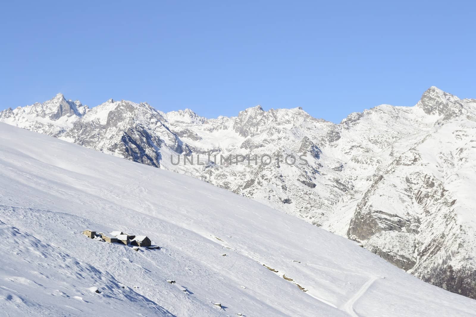 Winter landscape in the italian Alps with abandoned pasture huts covered by snow in scenic high altitude background (Gran Paradiso National Park).