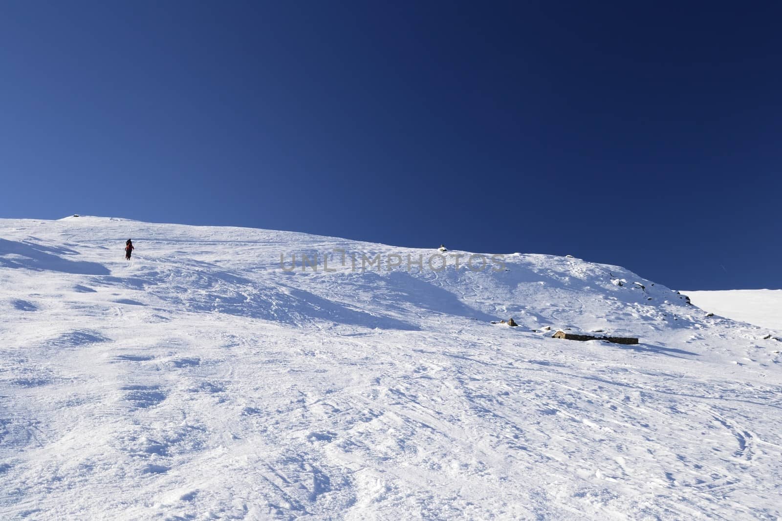 Alpinist hiking uphill by ski touring on the mountain ridge in powder snow with deep track in the foreground and scenic high mountain view in the background