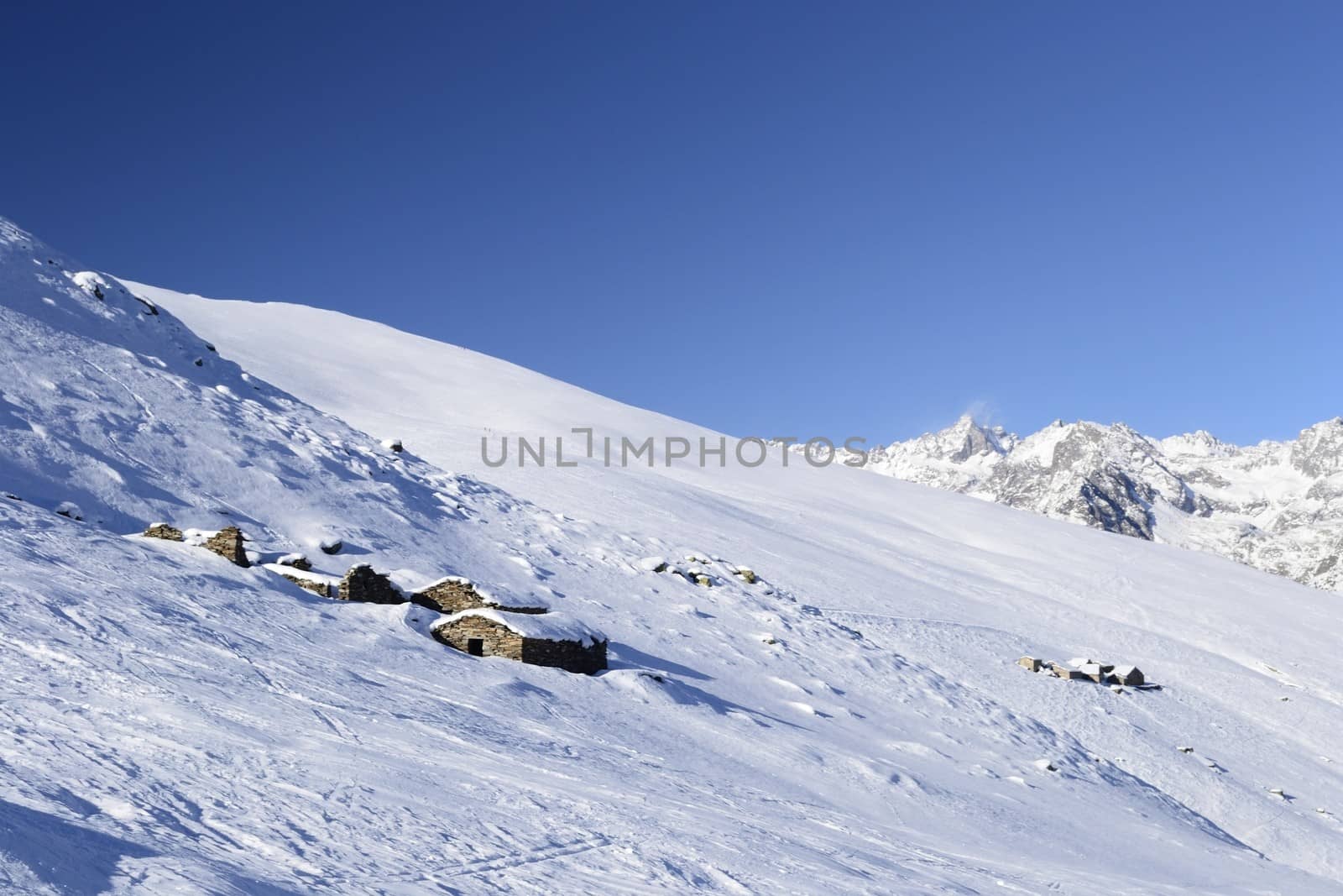 Winter landscape in the italian Alps with abandoned pasture huts covered by snow in scenic high altitude background (Gran Paradiso National Park).