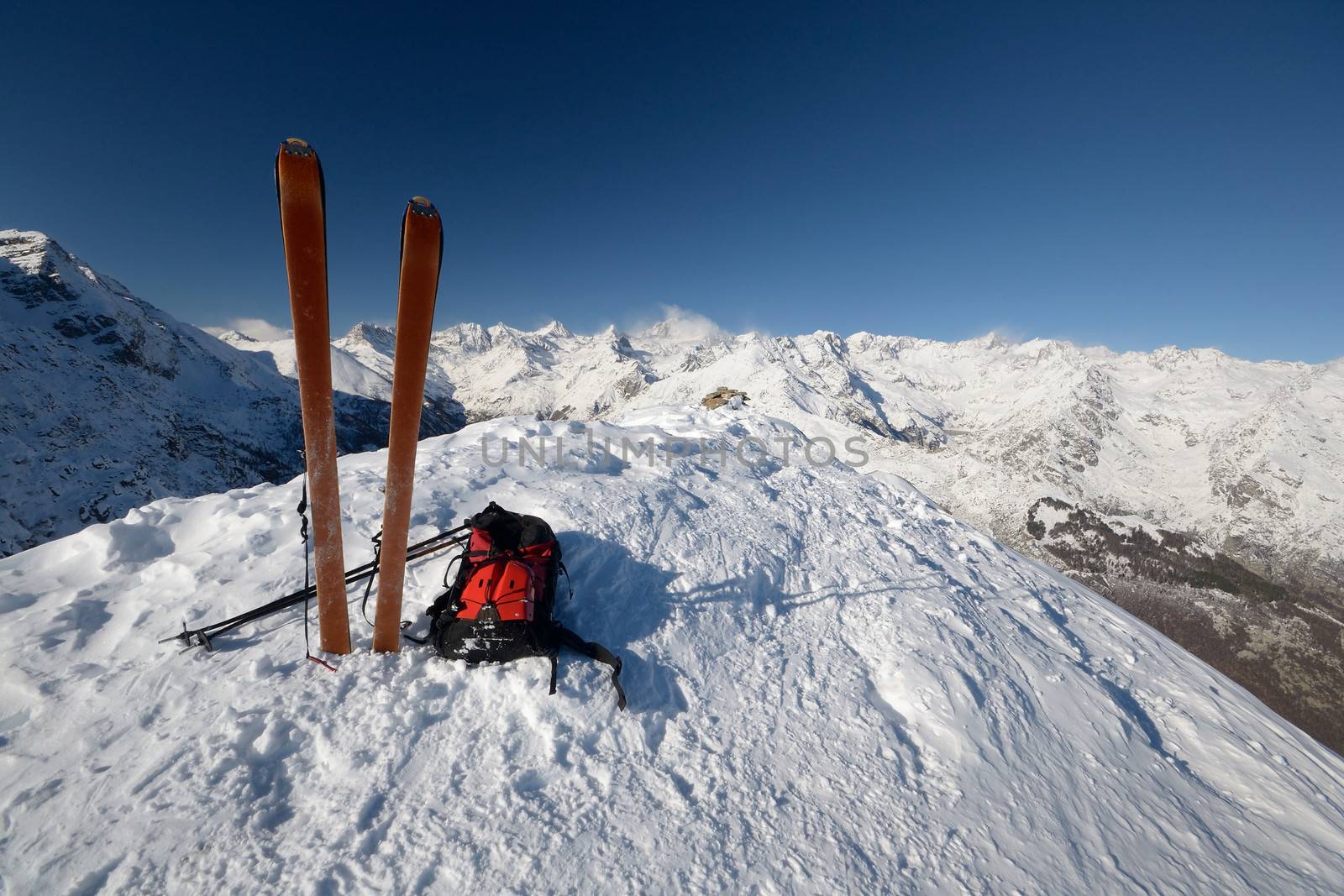 On the top of the mountain, pair of back country - tour ski and a backpack with avalanche safety tools. Scenic high mountain background (Gran Paradiso peak, 4061 m).