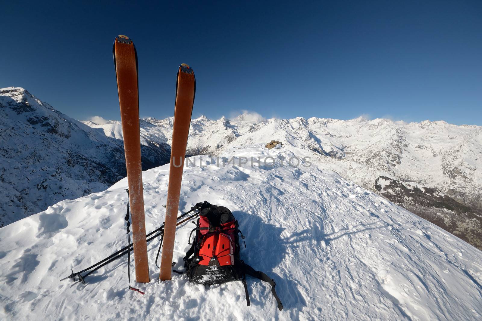 On the top of the mountain, pair of back country - tour ski and a backpack with avalanche safety tools. Scenic high mountain background (Gran Paradiso peak, 4061 m).