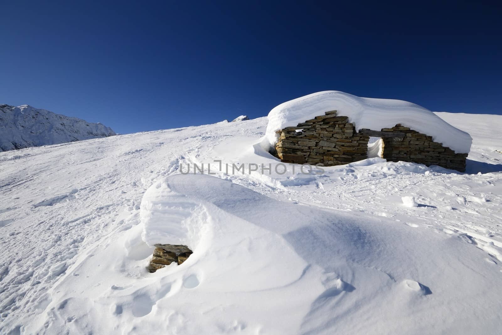 Winter landscape in the italian Alps with abandoned pasture hut covered by snow. Back country ski tracks.