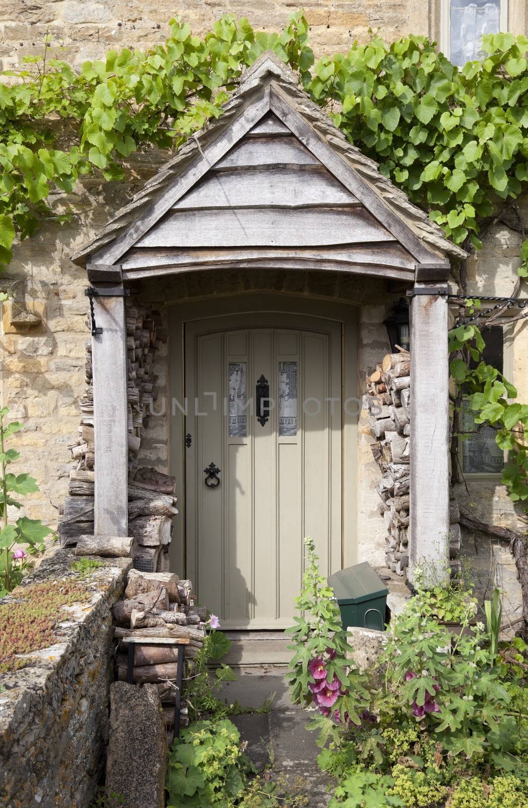 Pretty English cottage doorway with logs and flowers, Cotswolds, Gloucestershire, England.