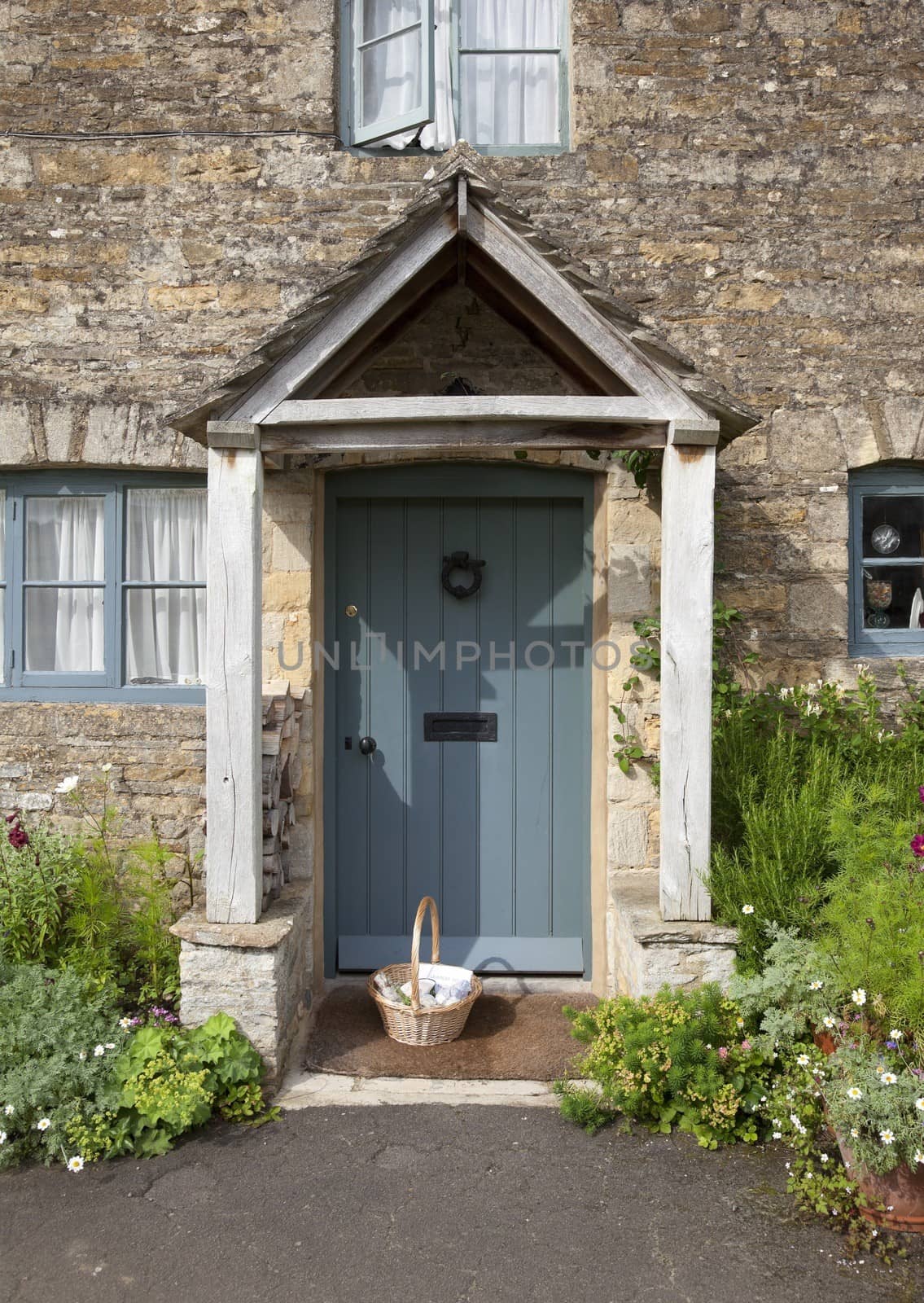 Pretty Cotswold cottage doorway with basket and flowers, Gloucestershire, England.