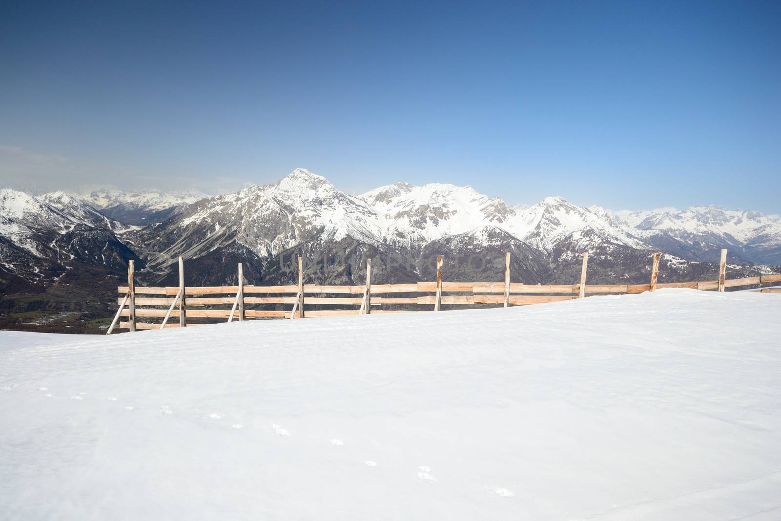 A wooden snow fence or avalanche fence with majestic view on the italian - french alpine arc in the background