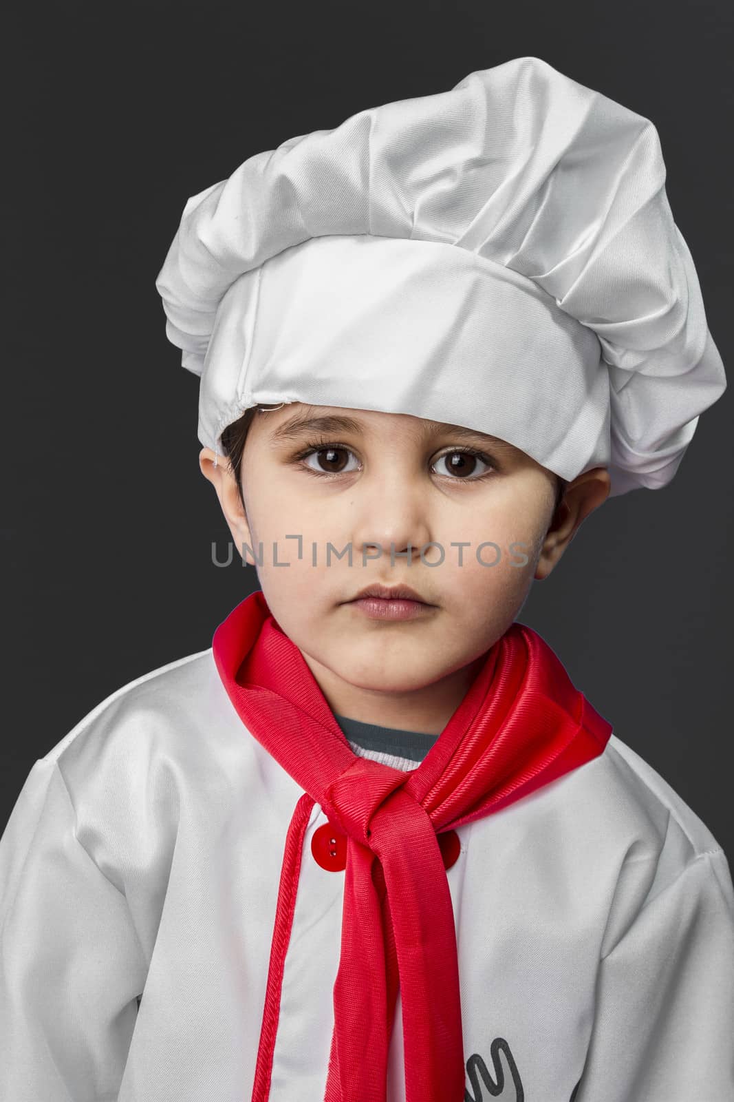 Little boy preparing healthy food on kitchen over grey background, cook hat