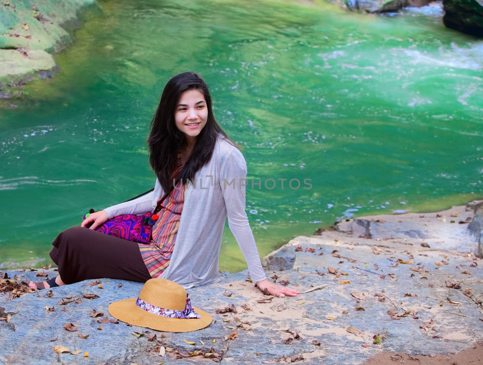 Biracial teen girl sitting next to river, smiling